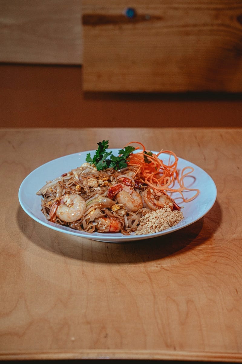 Pad thai with shrimp, carrot curls and crushed peanuts on a white plate