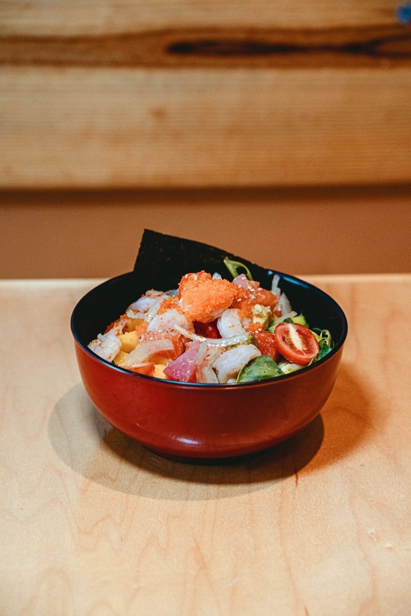 Red bowl of poké with shrimp, tobiko and a cherry tomato