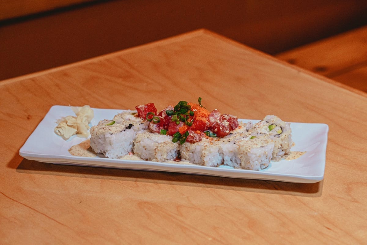 Sushi roll topped with diced tuna poké and green onion on a white plate